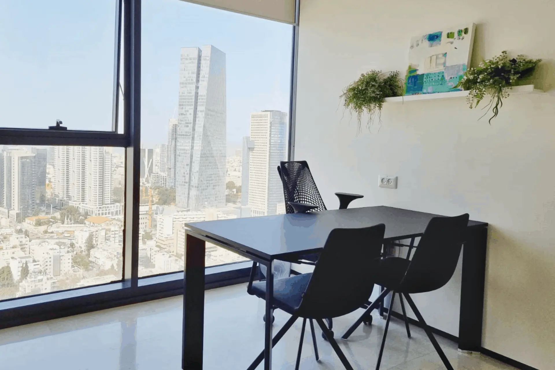 חדר עבודה מואר עם שולחן שחור וכיסאות מול נוף עירוני