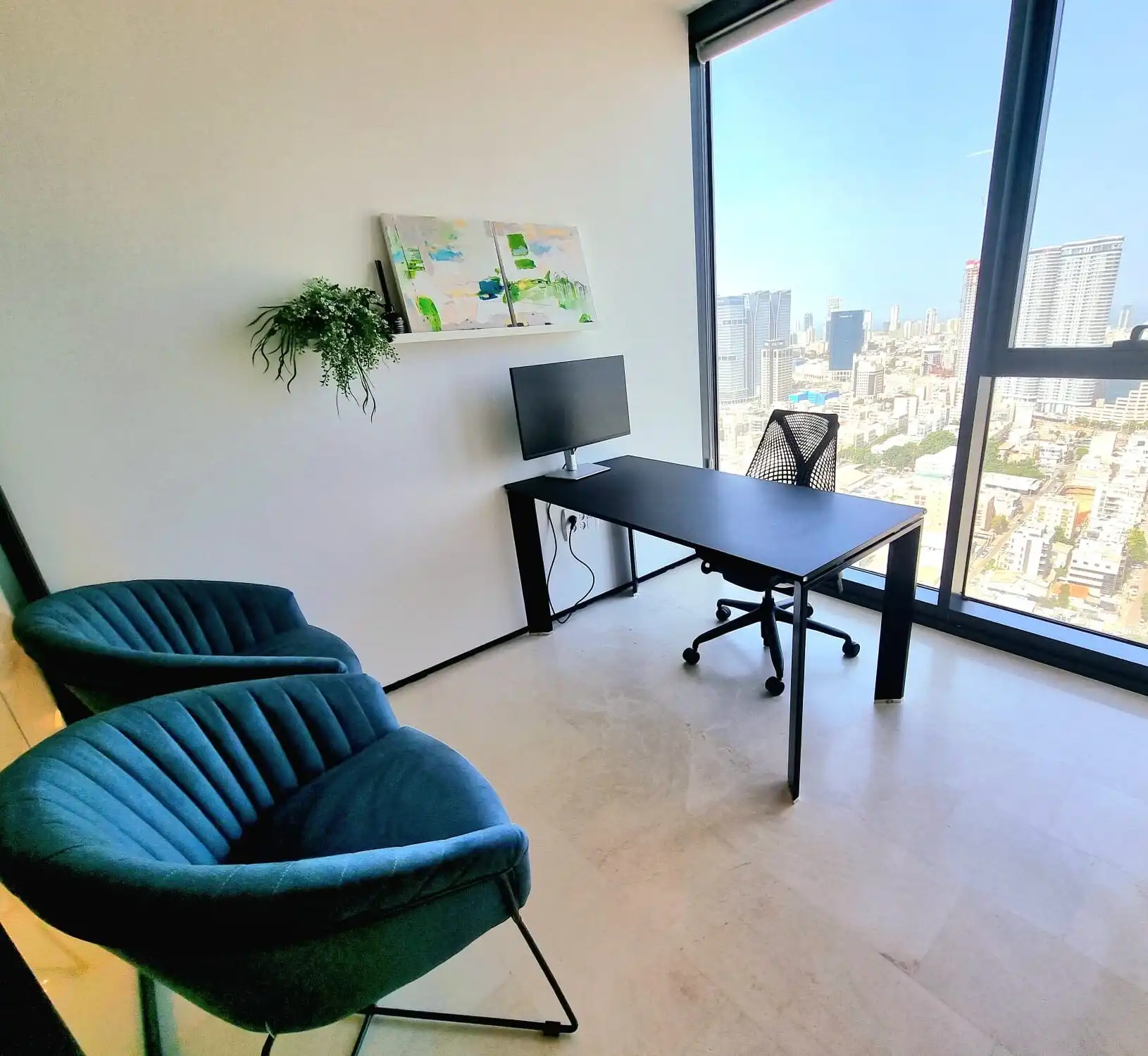 משרד פרטי מואר עם שולחן שחור מסך מחשב וכיסאות אורחים כחולים מול נוף עירוני