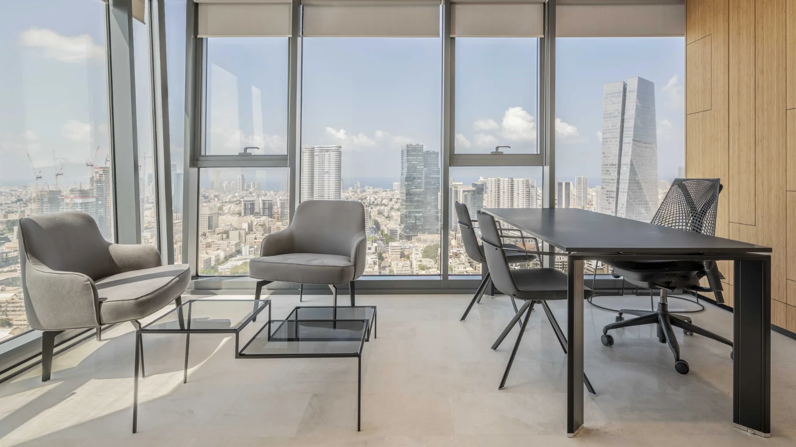 משרד מואר עם חלונות מהרצפה לתקרה ספות אפורות ושולחן עבודה שחור