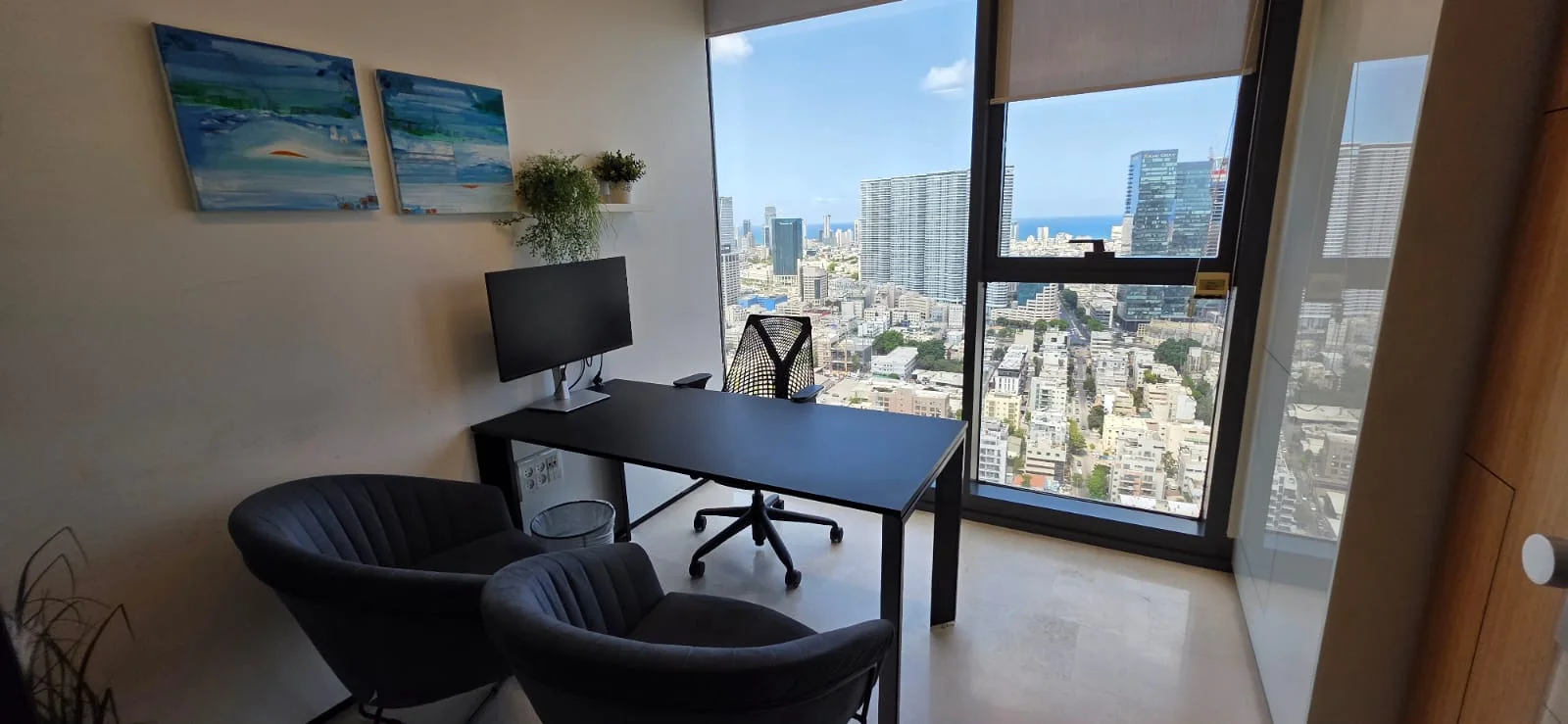 משרד מודרני עם שולחן עבודה ומסך ושתי כורסאות מול נוף עירוני