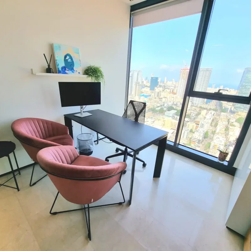 משרד פרטי מואר עם חלון גדול לנוף עירוני ושולחן שחור ושתי כורסאות ורודות